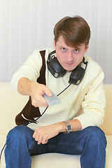 Image showing Person with remote control and ear-phones watches TV on sofa