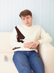 Image showing Young man sits on sofa with remote control