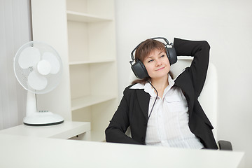 Image showing Young beautiful woman at office with ear-phones and listens to m