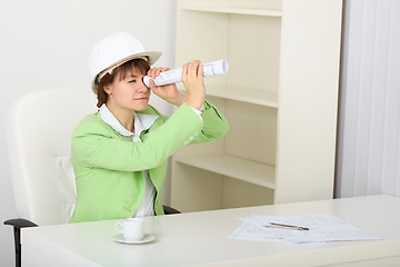 Image showing Young woman in helmet sits at table with draft in hands