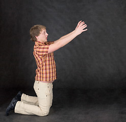 Image showing Amusing young man is kneeling and stretch hands to something