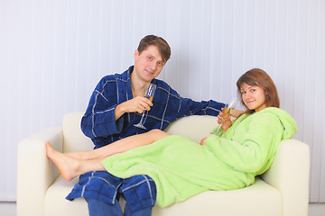 Image showing Young couple drinks sparkling wine on sofa in dressing gowns