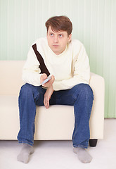 Image showing Young man sits on sofa with remote control