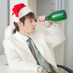 Image showing Drunk man in Christmas cap plays the fool with bottle