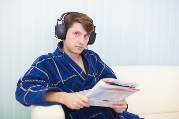 Image showing Man in big ear-phones on sofa reads newspaper