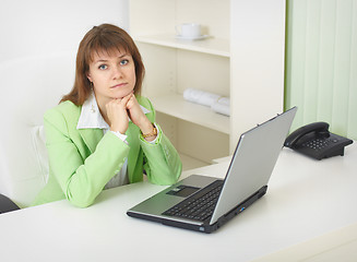 Image showing Young woman with laptop sits at table at light office