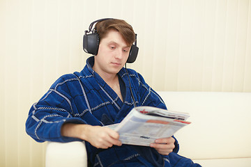 Image showing Man in big ear-phones on sofa reads journal