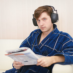 Image showing Person in big ear-phones on sofa reads newspaper