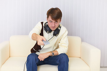 Image showing Man sits on sofa with earphones and remote control