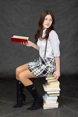 Image showing Schoolgirl sits on big pile of books against dark background