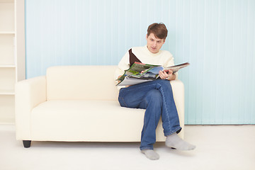 Image showing Young man sits on sofa with journal