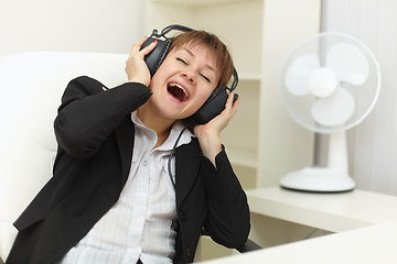 Image showing Young woman with ear-phones on head sings on a workplace