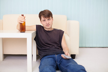 Image showing Man sits on floor with beer bottle in a hand