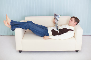 Image showing Young man reads magazine lying on couch