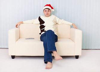 Image showing Young man in Christmas hat sits on sofa and watches TV