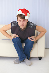 Image showing Young man in Christmas cap sits on sofa and watches TV