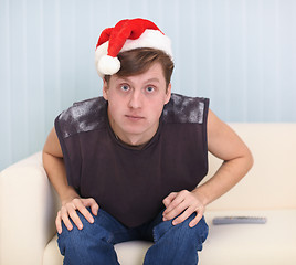 Image showing Young man sits on sofa in a red Christmas cap