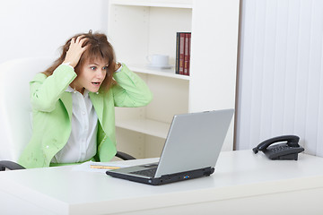 Image showing Scared woman sits on workplace with laptop