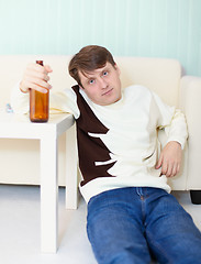 Image showing Drunken man sits on floor with beer bottle