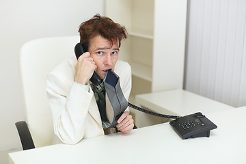 Image showing Confused tousled man speaks on phone and chews tie