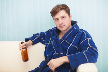 Image showing Young man in dressing gown sits on a couch with bottle