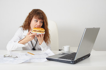 Image showing Person at office on workplace eats a hamburger