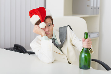 Image showing Young man in christmas hat cap with bottle sits at table