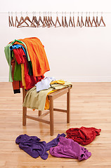 Image showing Messy clothes on a chair and empty hangers on the background