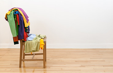 Image showing Wooden chair with messy clothes on it