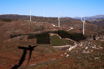 Image showing mountain where the trees draw a heart with windmills power,  on blue sky;