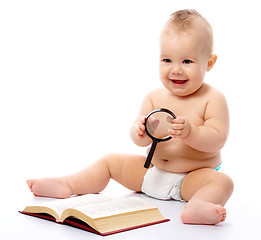 Image showing Little child play with book and magnifier