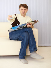 Image showing Man sits on sofa with newspaper and remote control