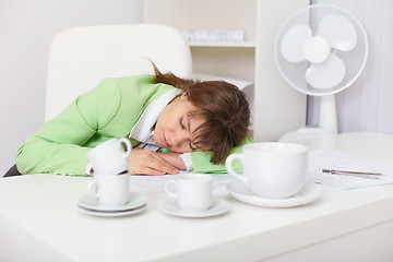 Image showing Tired woman sleeping on desk in the office among coffee cups