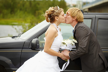 Image showing Bride and groom kissing near a car