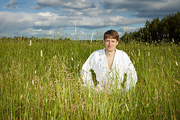 Image showing Young man in white kimono sits in grass