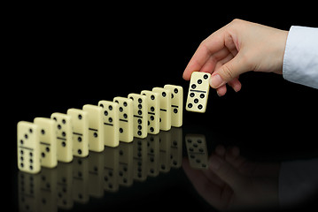 Image showing Hand builds a line of dominoes on black background