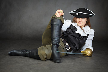 Image showing Iimpudent woman pirate lies with sabre on black background