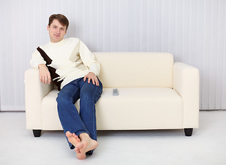 Image showing Young man sits on sofa and has rest