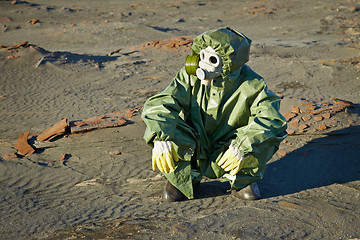 Image showing Scientist in protective suit and gas mask sitting on slag