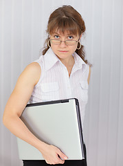 Image showing Serious girl holds closed laptop in hand