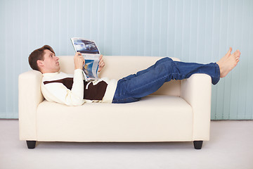 Image showing Young man lies comfortably on sofa with a newspaper