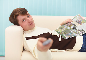 Image showing Smiling man, lying on couch with magazine and TV remote control