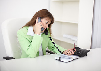 Image showing One girl sitting at desks and talking on phone