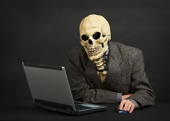 Image showing Terrible skeleton sits at black office with laptop