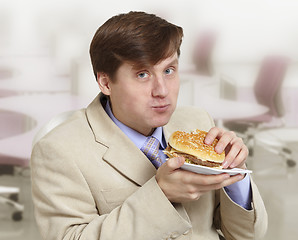 Image showing Young funny businessman eats a hamburger