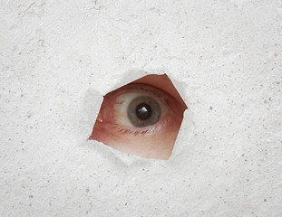 Image showing Eye looking through hole in gray wall