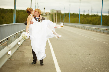 Image showing Groom carries his bride in his arms on bridge