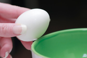 Image showing Hand holding an egg over green bowl