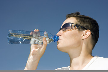 Image showing The girl a unisex drinks water from a bottle
