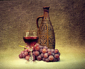 Image showing Dark Still Life - clay bottle, glass and grapes